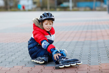 Little school kid boy skating with rollers in the city. child in protection safety clothes. Active...