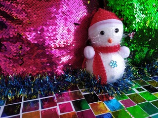 Toy snowman in red hat and scarves on a colorful shiny background