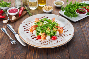 Fresh healthy avocado and shrimps salad with arugula, tomatos and mozzarella cheese on wooden background, cooking concept with ingredients