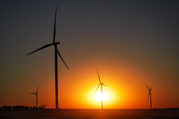 Wind turbines and agricultural field at sunset. Energy production, clean and renewable energy.