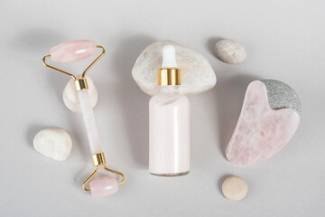 Crystal rose quartz facial roller, massage tool Gua sha and anti-aging collagen, serum in glass bottle on stones, grey background. Facial massage for natural lifting, Beauty concept Top view