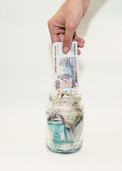 a man puts a bill in a glass jar filled with paper money