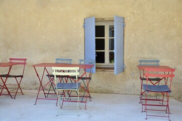 Fototapeta na wymiar Vintage colorful chairs and tables in front of an old yellow house wall, open blue shutters, patio