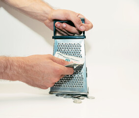 men's hands rub a banknote on a grater, and iron coins lie below