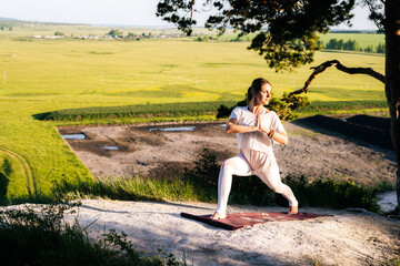 Concentrated young woman doing warrior yoga asana pose on top of rock background of beautiful landscape. Girl with flexible body performing Virabhadrasana. Concept of practicing yoga alone outdoor.