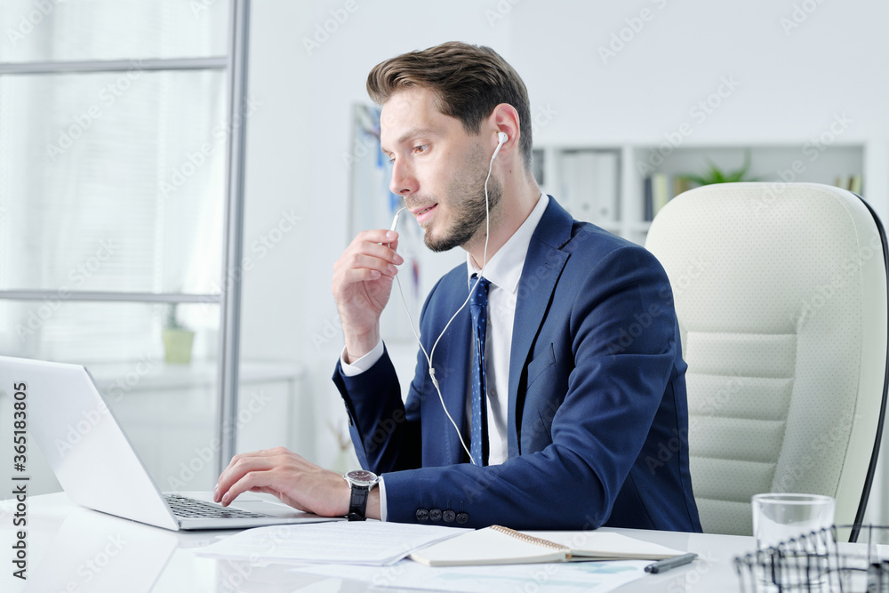 Aufkleber busy young manager with stubble sitting at desk and talking through earpiece while answering questio