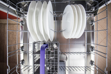 Stacked plates in dishwasher to be cleansed of stains with hot water, soap and detergent for shiny household using electric modern dishwasher