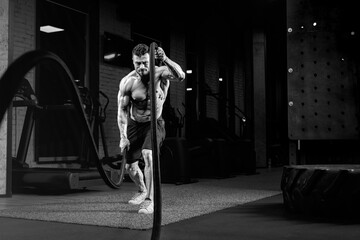 Fototapeta na wymiar Monochrome portrait of shirtless man training with ropes.