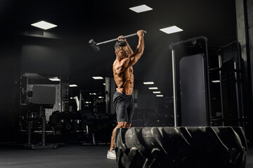 Muscular man hitting giant wheel with sledgehammer.