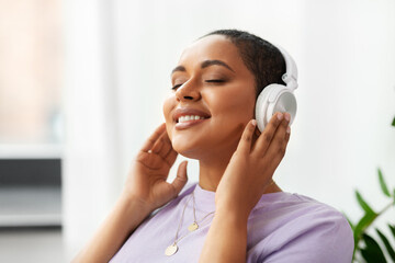 people, technology and leisure concept - happy young african american woman in headphones listening to music at home