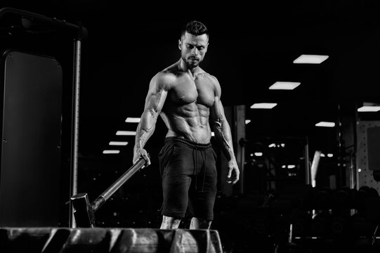 Muscular bodubuilder holding sledgehammer on tire.