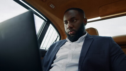 African man looking laptop screen. Businessman working computer at car