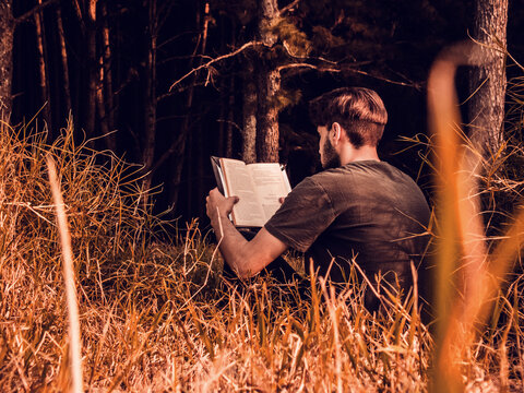 Man sitting on grass reading a book at sunset -autumn afternoon 