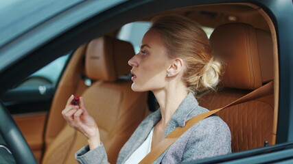 Fototapeta na wymiar Closeup woman applying red lipstick in vehicle. Sexy woman sitting in luxury car