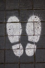 Portrait image of social distancing footsteps stencilled onto block paving