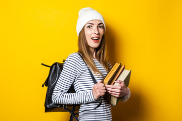 Beautiful young girl with a backpack holds books on a yellow background.