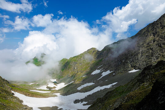 high mountain peaks among the clouds. wonderful summer landscape of fagaras ridge with some snow on hills. cloudy weather with blue sky