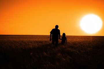 The silhouette of a man and a little girl in a field during sunset. Toned