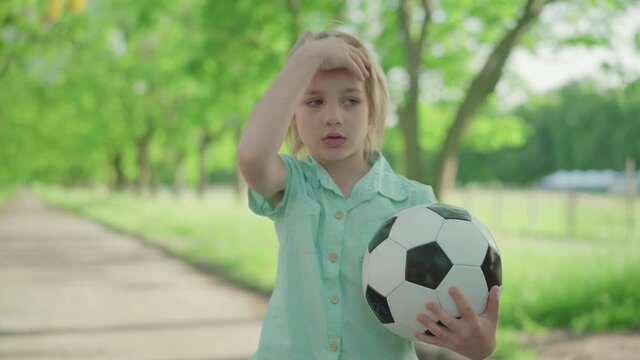 Middle shot of cute blond boy with soccer ball yelling at joyful sister running around. Dissatisfied brother arguing with sibling in sunny summer park. Conflict, family relationship.
