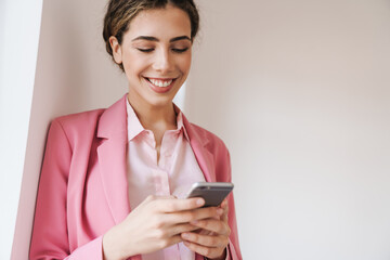 Photo of young cheerful woman using mobile phone while posing on camera