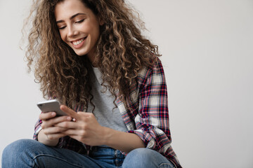 Fototapeta premium Photo of pleased woman smiling and using cellphone while sitting