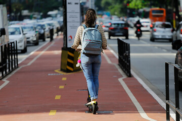 A young woman rides a shared electric scooter along the bike path of Paulista avenue, Sao Paulo...