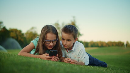 Children using smartphone in park. Siblings lying on green grass in meadow