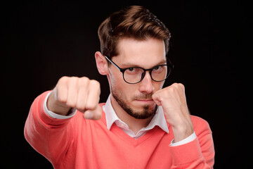 Portrait of serious confident young man in eyeglasses throwing punch while protecting himself