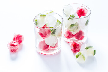 Cocktail glasses with berries in ice cubes on white table