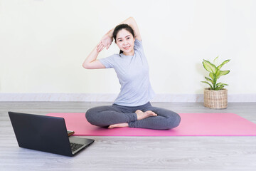 Fototapeta premium Fitness training online, young asian woman in casual sportswear doing morning exercises and watching videos on laptop, healthy lifestyle workout at home concept.
