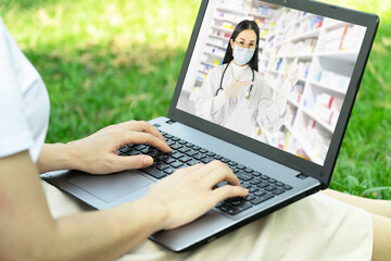 Online medical consultation and support doctor concept.Young asian woman or customer having video chat with doctor in Pharmacy on laptop computer while sitting in the park.