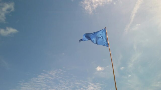 Blue triangle flag fluttering in the wind against blue sky at a beach in France. It indicates a bathing area.