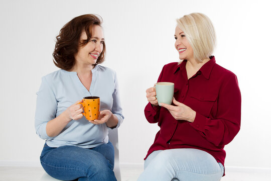 Two healthy and beautiful middle aged women drinking tea and talking isolated on white background. Woman support woman. Happy menopause concept.