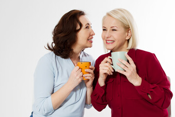 Two healthy and beautiful middle aged women drinking tea and talking isolated on white background. Woman support woman. Happy menopause concept.