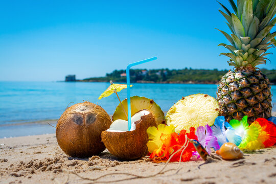 Drink made with coconut surrounded by pineapple and summer objects on the beach