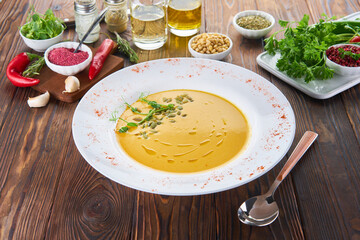 Organic vegan pumpkin creme soup on wood table with ingredients, healthy diet food concept