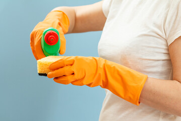 Woman holding a bottle of dishwashing liquid and a sponge on a blue background.