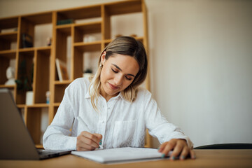 Portrait of a beautiful female writer working. Businesswoman writing with pen in notebook.