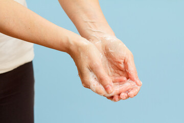 Fototapeta premium Woman washing hands with soap on blue background.