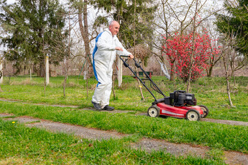 Farmer in protective clothing is mowing a lawn in a garden with a petrol lawn mower
