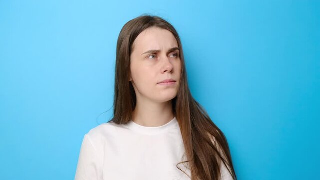 Confused young woman isolated on blue studio background looking around as if searching problem solution, thinking idea with doubtful uncertain expression, dressed in white t-shirt, difficult decision