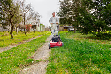 Farmer in protective clothing is mowing a lawn in a garden with a petrol lawn mower