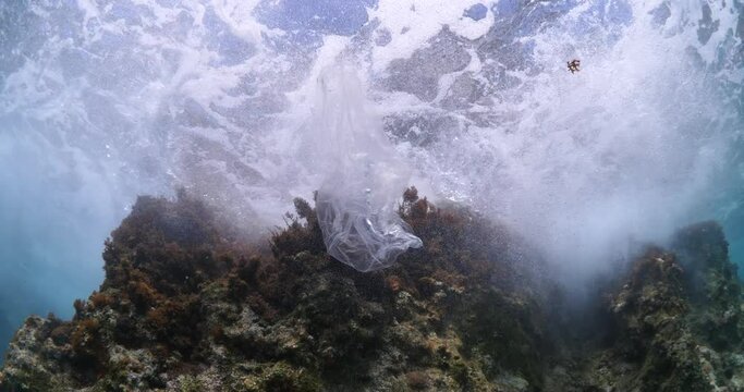 plastic bag underwater bad for fish with sun rays water waves hit to rocks background ocean pollution