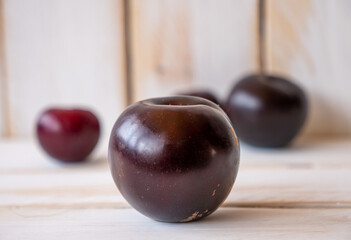 Some dark ripe plums on a white wooden wall and table
