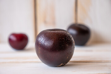 Some dark ripe plums on a white wooden wall and table