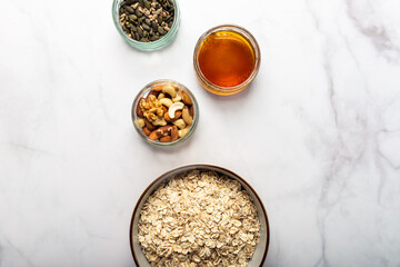 Ingredients for healthy homemade granola with Gluten Free Rolled oats or porridge oats, variety of chopped nuts and seeds, and maple syrup. Preparation for cooking at home. Marble background