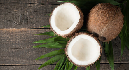 Ripe half cut coconut with green leaves on a wooden background.