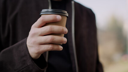 Man hand bringing takeaway coffee to lips. Guy hand holding paper cup outdoors.