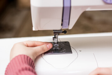 The girl is threading the needle of a sewing machine. Close plan. White sewing machine. Sewing content.