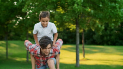 Fototapeta premium Boy jumping on man back in field. Portrait of happy father carrying son on back